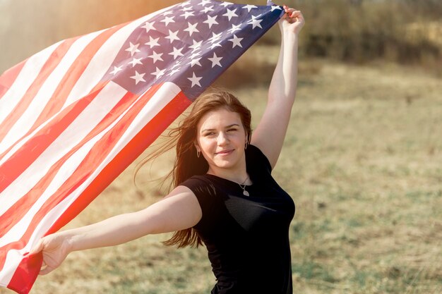 Mujer de pie en el campo y sosteniendo la bandera estadounidense
