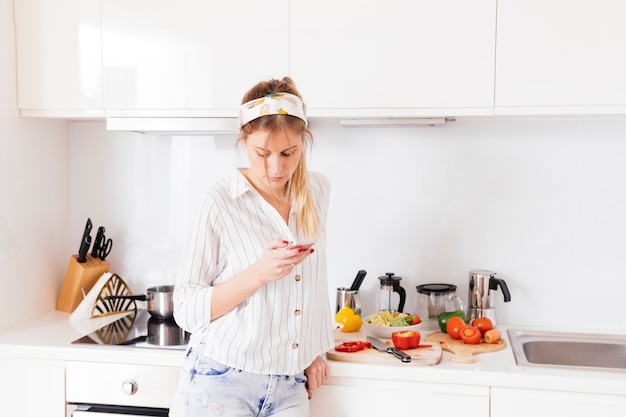Mujer de pie cerca de la encimera de la cocina usando un teléfono móvil