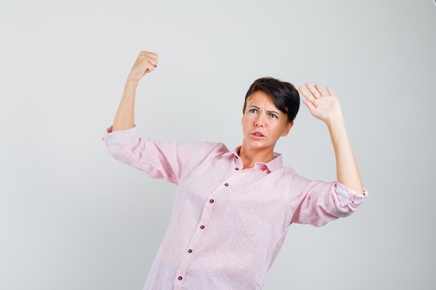 Mujer de pie para defenderse con camisa rosa y luciendo preocupada. vista frontal.