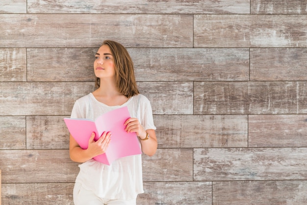 Mujer de pie delante de la pared con libro rosa