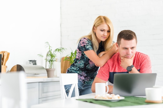 Mujer de pie detrás del hombre contemplado que trabaja en la computadora portátil