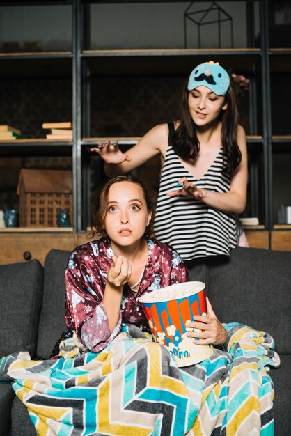 Mujer de pie detrás de su amiga viendo la televisión