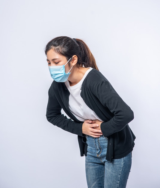 Una mujer de pie con dolor de estómago y presiona su mano sobre su estómago.