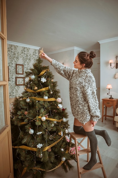 Mujer de pie en la escalera y decorar el árbol de navidad