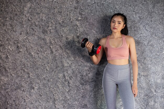 Mujer de pie haciendo ejercicio con una pesa roja en el gimnasio.