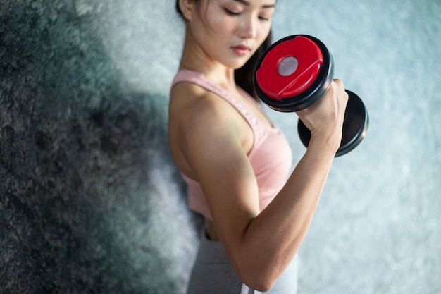 Mujer de pie haciendo ejercicio con una pesa roja en el gimnasio.