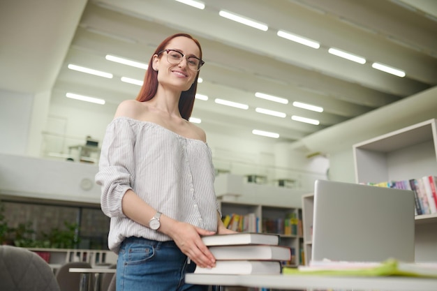 Foto gratuita mujer de pie junto a la mesa con libros mirando a la cámara