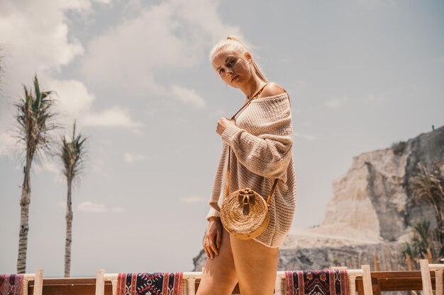 Mujer de pie junto a palmeras y rocas bajo un cielo nublado