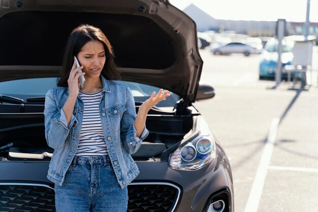 Mujer de pie junto a su coche roto