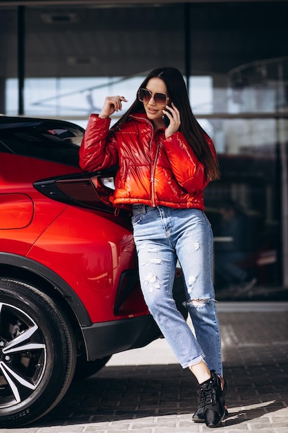 Mujer de pie junto a su nuevo coche rojo y hablando por teléfono