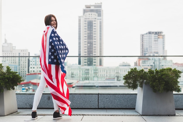 Mujer de pie en media vuelta con gran bandera de Estados Unidos