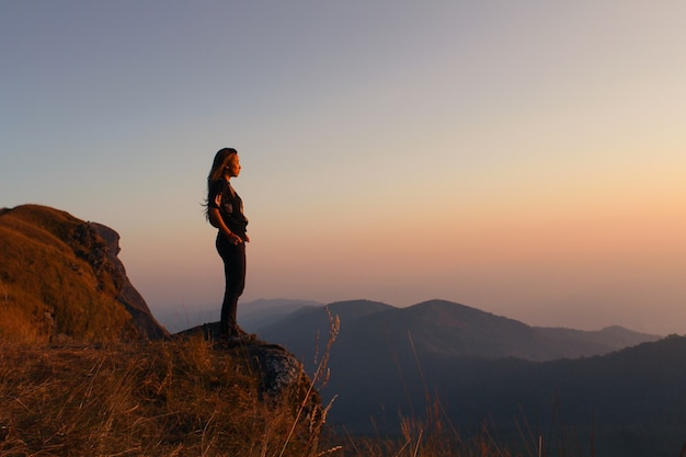 Mujer de pie en una montaña mirando al atardecer