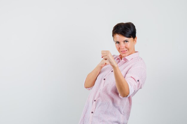 Mujer de pie en pose de lucha en camisa rosa y mirando confiado, vista frontal.