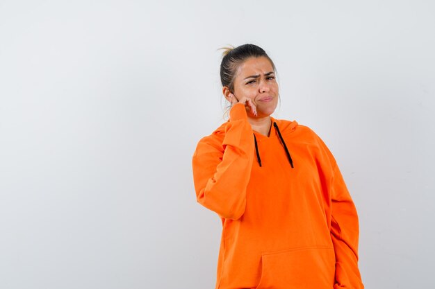 Mujer de pie en pose de pensamiento en sudadera con capucha naranja y mirando molesto