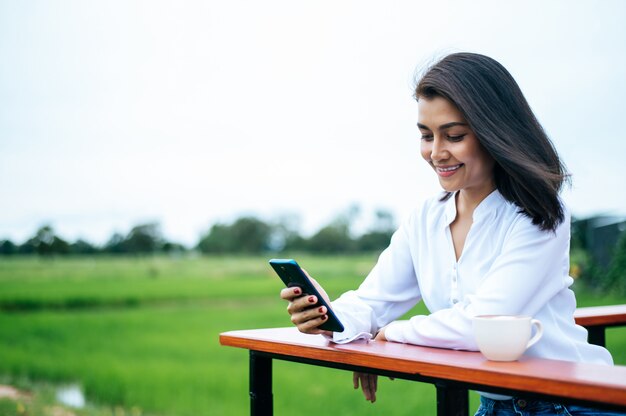 Mujer de pie en un teléfono inteligente y tomar una taza de café