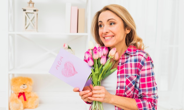 Foto gratuita mujer de pie con tulipanes y tarjeta de felicitación
