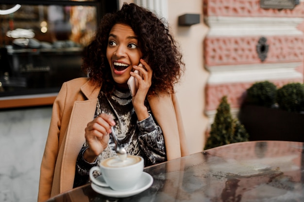 Mujer con piel negra y sonrisa sincera hablando por teléfono y disfrutando