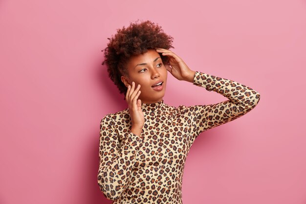 Mujer de piel oscura con cabello rizado, mira a un lado pensativamente, vestida con un elegante traje de leopardo