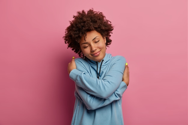 Foto gratuita mujer de piel oscura complacida con cabello afro, se abraza a sí misma