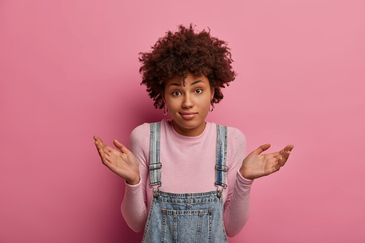 Foto gratuito mujer de piel oscura cuestionada insegura levanta las manos con expresión confusa, perpleja para dar una respuesta a una pregunta difícil, viste un atuendo casual, aislado sobre una pared rosa. percepcion humana