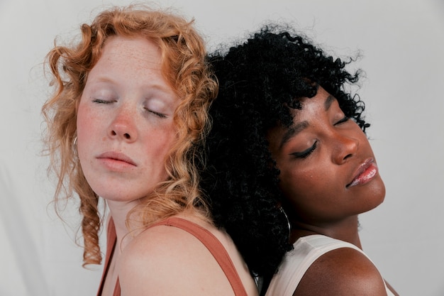 Mujer de piel oscura inclinada a su amiga rubia que duerme espalda con espalda