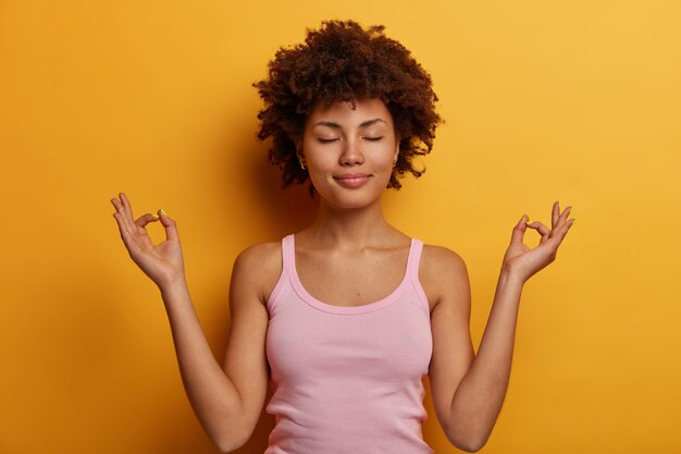 Mujer de piel oscura pacífica con peinado afro viste camiseta rosa