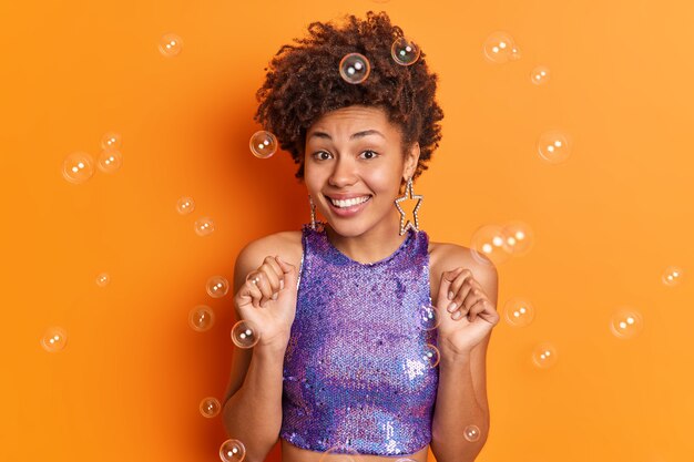 Mujer de piel oscura positiva con cabello afro rizado aprieta los puños celebra algo que disfruta de una ocasión especial en la vida