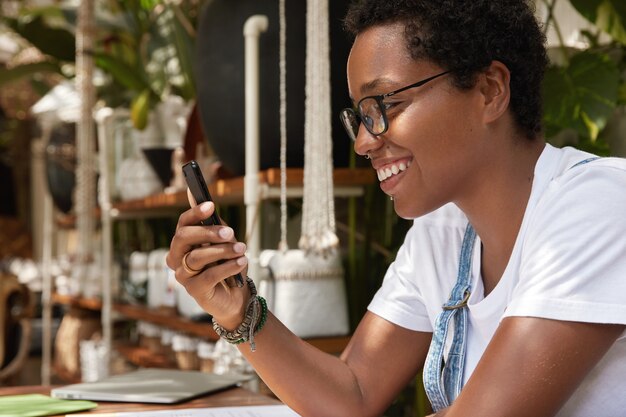 Mujer de piel oscura positiva emocionada con buenas noticias recibiendo notificación en el teléfono inteligente