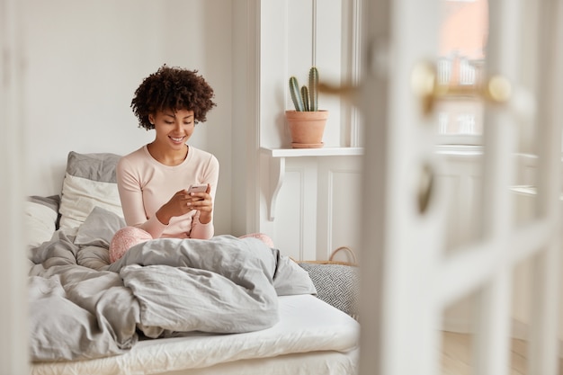 Mujer de piel oscura positiva lee la publicación de Internet en el sitio web a través de un teléfono celular