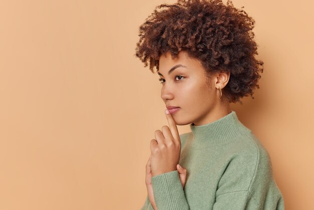 mujer piensa en algo con expresión misteriosa intrigada viste un jersey casual aislado en un espacio de copia en blanco beige para su anuncio.