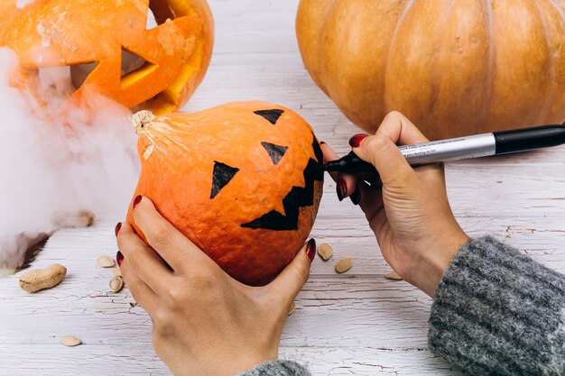 La mujer pinta una cara en una pequeña calabaza naranja para Halloween