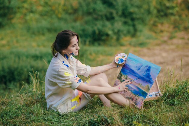 Mujer pintando un cuadro sentada sobre la hierba