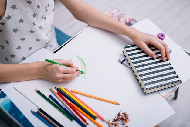 Mujer pintando sobre papel en mesa con set de lápices y cuaderno