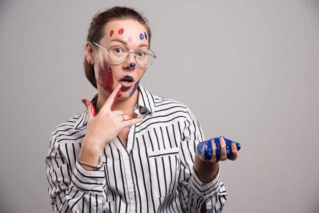 Mujer con pinturas en la cara y gafas sobre fondo gris