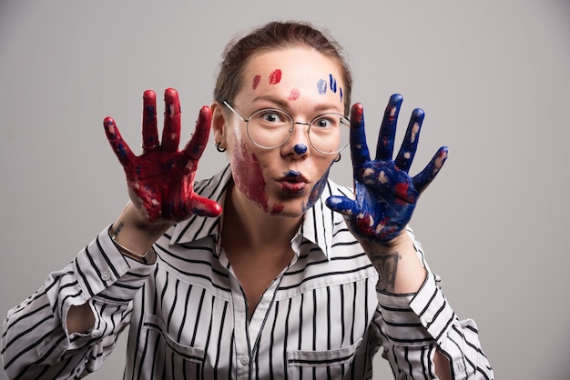 Mujer con pinturas en la cara y gafas sobre fondo gris