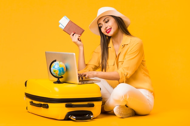 Mujer planeando un viaje en la computadora portátil mientras sostiene boletos de avión y pasaporte