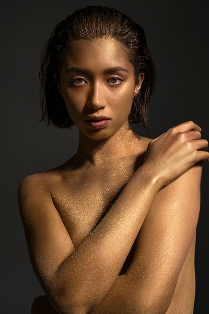 Foto gratuita mujer de plano medio posando con pintura corporal dorada
