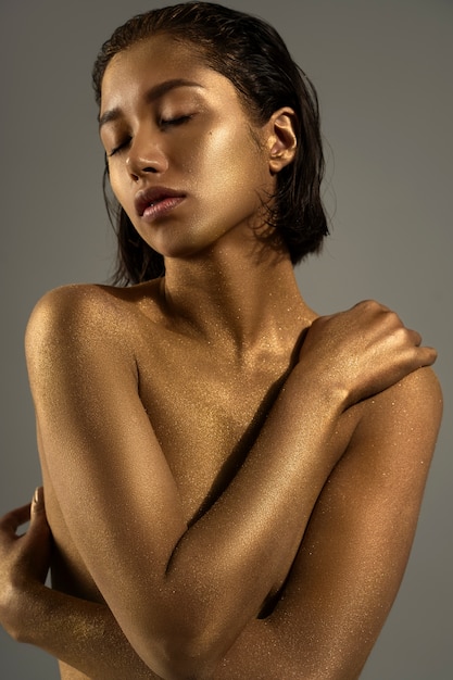 Mujer de plano medio posando con pintura corporal dorada