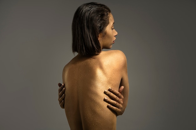 Mujer de plano medio posando con pintura corporal dorada