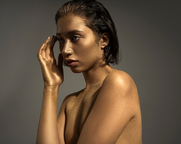 Mujer de plano medio posando con pintura corporal dorada