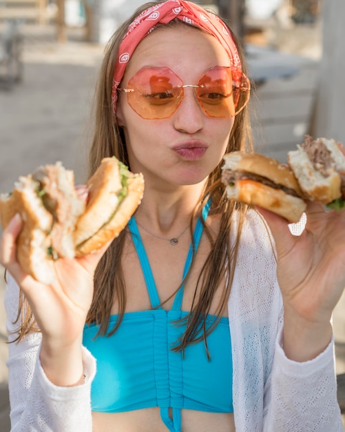 Mujer en la playa comiendo muchas hamburguesas