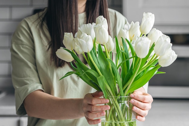 Mujer poniendo un ramo de flores de tulipán blanco en un jarrón en la cocina