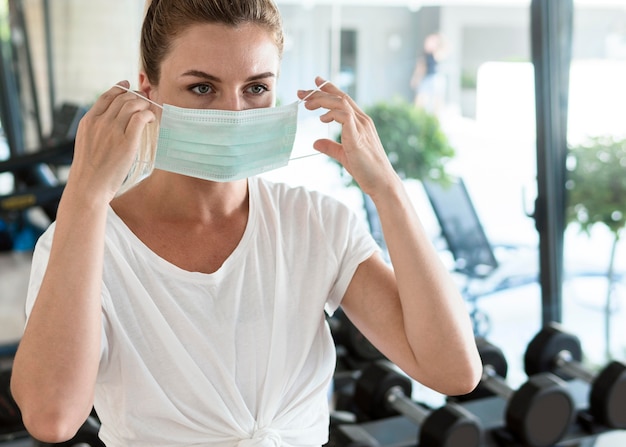 Mujer poniéndose máscara médica en el gimnasio