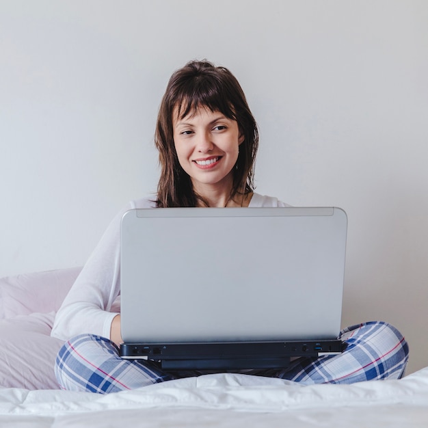 Foto gratuita mujer con portátil en la piernas sentada en la cama