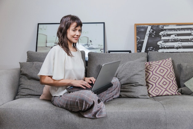 Mujer con portátil sentada en sofá en casa