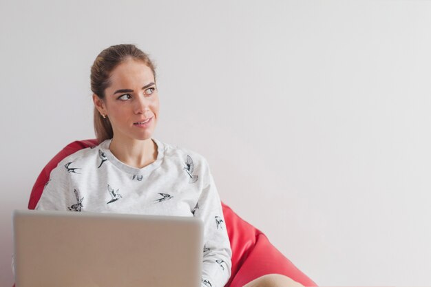 Mujer con portátil en sofá mirando a lado