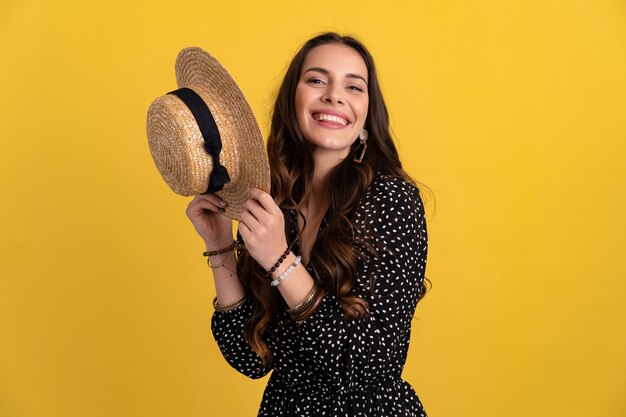 Mujer posando aislada en amarillo con vestido negro punteado y sombrero de paja con estilo boho