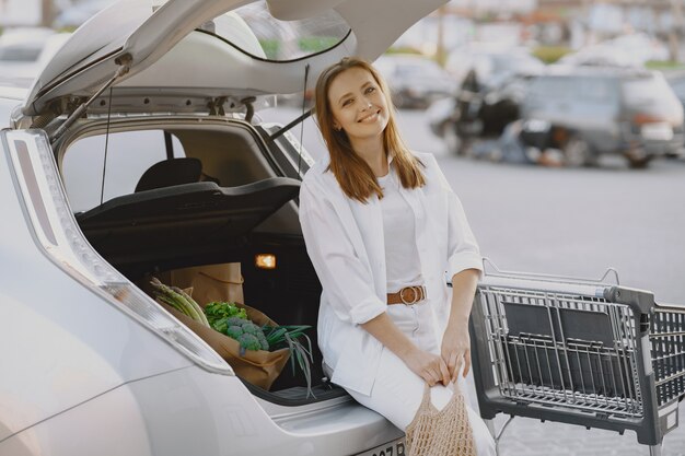 Mujer posando con una bolsa de compras en su automóvil