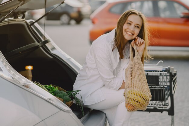 Mujer posando con una bolsa de compras en su automóvil