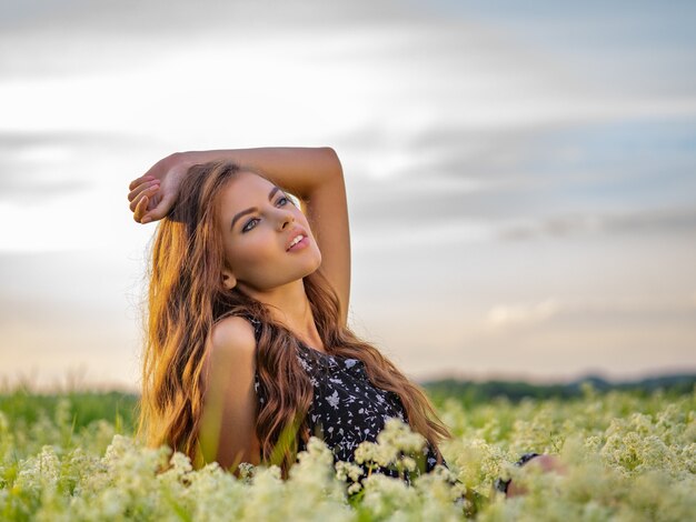 Mujer posando en un campo de flores blancas de lavanda. Retrato de niña adulta joven sentada al aire libre en un campo de flores blancas.